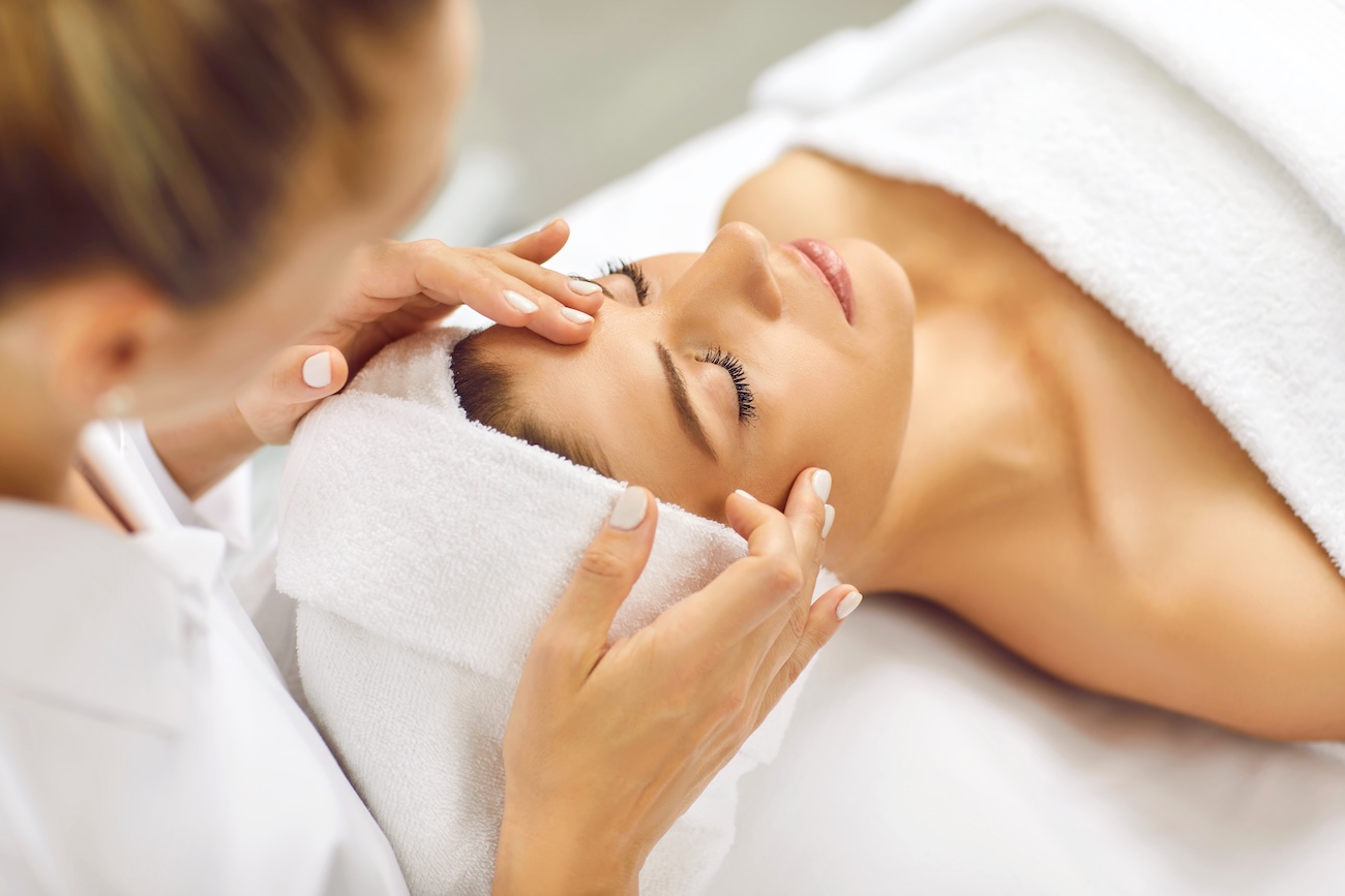 Portrait of pretty relaxed young woman lying with closed eyes having facial massage in spa salon. Female client enjoy receiving skin care procedure treatment. Wellness and beauty day concept.