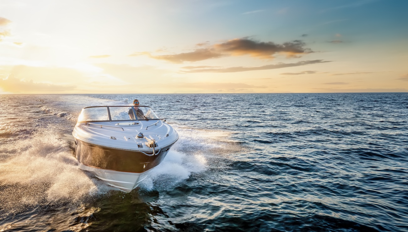 Aerial front view of a motor boat cruising with speed over the ocean during sunset time with copy space